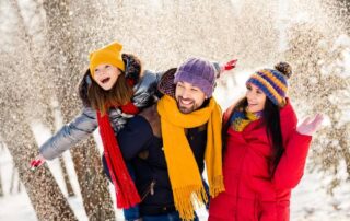 A family in coats and scarves walking through a snowy forest