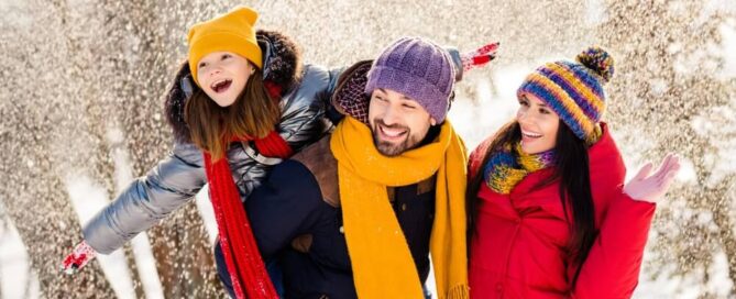 A family in coats and scarves walking through a snowy forest