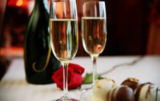 A bottle of champagne, two glasses, a rose, and chocolate covered strawberries on a table as part of one of Whiteface Lodge's Lake Placid getaway packages