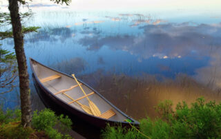 A canoe floating on a calm lake with clouds reflecting off the water in Lake Placid